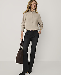 A woman wearing a beige quarter-zip sweater and dark flared jeans stands holding a brown tote bag against a plain white background. carousel Product Image 3