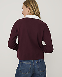 A woman wearing a maroon sweater with a white collar and blue jeans stands against a plain light gray background. carousel Product Image 2