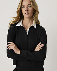 A blonde woman wearing a black long-sleeved shirt with a white collar stands with her arms crossed against a plain, light-colored background. carousel Product Image 1