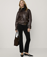 A woman wearing a brown leather jacket, black trousers, and black heels stands against a plain white background while holding a brown handbag. carousel Product Image 1