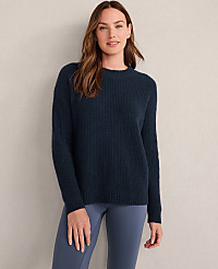 A woman in a light gray ribbed sweater stands against a textured, neutral background. carousel Product Image 1