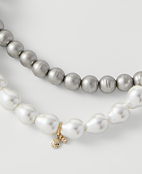 Two strands of pearls, one grey and one white with a small gold charm, rest against a plain light grey background. carousel Product Image 2