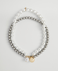 Two strands of pearls, one white and baroque and the other grey and round, are laid out in an oval shape against a plain white background. carousel Product Image 1