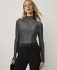 A blonde woman wearing a shimmering grey mock-neck top and black trousers stands against a plain white background. carousel Product Image 1
