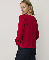 A woman wearing a red long-sleeved blouse and dark blue jeans stands against a plain, light-colored background. carousel Product Image 2