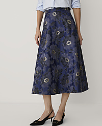 A person wearing a light blue shirt and a navy blue floral skirt with black heels stands against a plain white background. carousel Product Image 2
