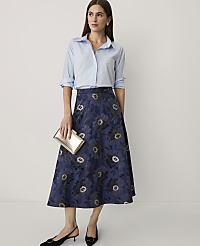 A woman wearing a light blue button-down shirt and a navy floral midi skirt stands against a plain white background. carousel Product Image 1