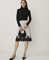 A woman wearing a black turtleneck and a polka-dot skirt with lace trim stands against a plain white background. carousel Product Image 1