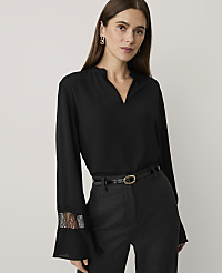 A woman wearing a black blouse and dark grey trousers stands against a plain, light-colored background. carousel Product Image 1