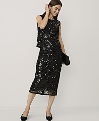 A woman wearing a black sequined two-piece outfit and holding a clutch stands against a plain, light-colored background. carousel Product Image 1