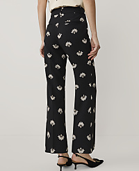 A person stands facing away from the camera wearing black floral trousers and black heels against a plain light grey background. carousel Product Image 3