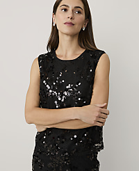A woman wearing a black sequined sleeveless top stands with her arms crossed against a plain, light-colored background. carousel Product Image 1