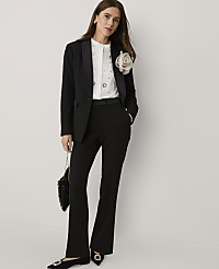 A woman wearing a black suit with a white embellished shirt and a large floral brooch stands against a plain white background. carousel Product Image 3