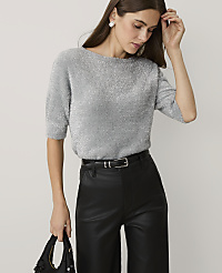 A woman wearing a shimmering silver sweater and black leather trousers stands against a plain light gray background. carousel Product Image 1