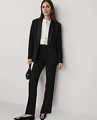 A woman wearing a black suit and white blouse stands against a plain white wall. carousel Product Image 1