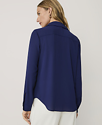 A woman wearing a navy blue long-sleeved blouse and white trousers stands against a plain light grey background. carousel Product Image 2