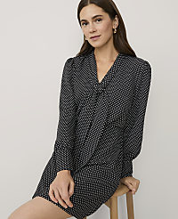 A woman wearing a black and white polka-dot dress sits on a wooden stool against a plain light gray background. carousel Product Image 3