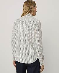 A woman wearing a white polka-dot shirt and dark blue pants stands against a plain light gray background. carousel Product Image 2