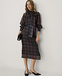 A woman wearing a red and black plaid dress and black heels stands against a plain white wall. carousel Product Image 1