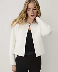 A woman wearing a white cardigan with a jeweled collar and black trousers stands against a plain light gray background. carousel Product Image 1