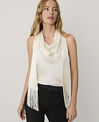 A woman wearing a cream-colored cowl-neck top and a matching fringed scarf stands against a plain light gray background. carousel Product Image 1