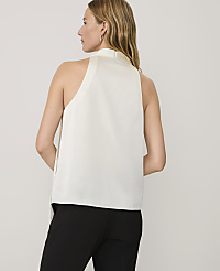 A woman wearing a white sleeveless top and black trousers stands against a plain light gray background. carousel Product Image 2
