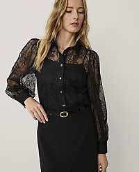 A woman wearing a black lace blouse and black trousers stands against a plain, light-colored background. carousel Product Image 1