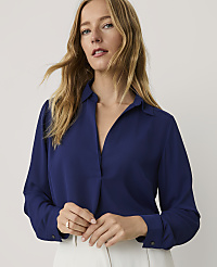 A blonde woman wearing a royal blue button-down shirt and white trousers stands against a plain, light-colored background. carousel Product Image 1