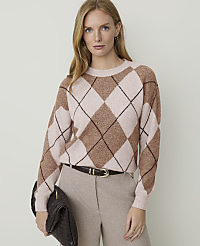 A woman in a tan argyle sweater and matching pants holds a dark brown clutch in front of a plain beige background. carousel Product Image 1