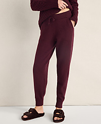 A person wears burgundy knit joggers and fuzzy brown slippers against a plain, light-colored wall. carousel Product Image 2