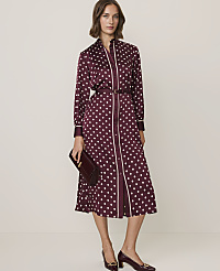 A woman in a burgundy polka dot dress with a pussy bow stands against a plain, light-colored background. carousel Product Image 1