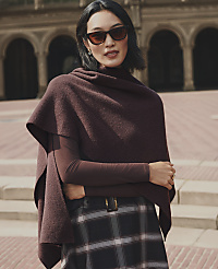 A woman wearing a burgundy wrap and plaid skirt stands in the foreground against a background of arched stone architecture. carousel Product Image 2