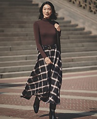 A woman wearing a brown turtleneck and a plaid skirt walks across a brick plaza in front of a large set of stone stairs. carousel Product Image 4