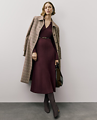 A woman wearing a burgundy ribbed dress, a plaid coat, and dark boots stands against a plain, light-colored wall and grey floor. carousel Product Image 5