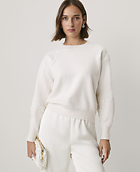 A woman wearing a white lace-detailed sweater and matching trousers stands against a plain, light-colored background. carousel Product Image 1