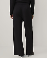 A person wearing a black long-sleeved top and wide-leg black trousers stands against a plain, light-colored background. carousel Product Image 3