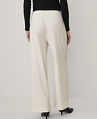 A person wearing a black long-sleeved top and wide-leg cream trousers stands against a plain light gray background. carousel Product Image 3