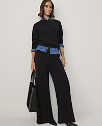 A woman wearing a black sweater over a blue denim shirt and wide-leg black trousers stands against a plain white background. carousel Product Image 1