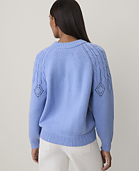 A woman seen from behind wears a light blue knit sweater and white pants against a plain, light-colored background. carousel Product Image 2