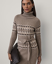 A woman wearing a brown patterned turtleneck knit dress and holding a dark woven clutch stands against a plain light gray background. carousel Product Image 3