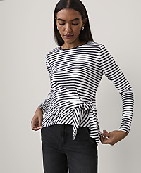 A woman wearing a navy and white striped long-sleeve top with a tie-front detail and black jeans stands against a plain white background. carousel Product Image 1