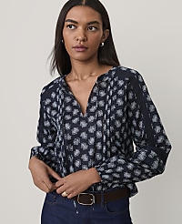 A woman wearing a navy blue floral print blouse and blue jeans stands against a plain, light-colored background. carousel Product Image 1