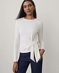 A woman wearing a white long-sleeved tie-front top and dark blue jeans stands against a plain light gray background. carousel Product Image 1