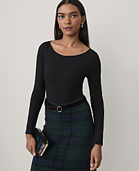 A woman wearing a black long-sleeved top and a green plaid skirt stands against a plain, light-colored background. carousel Product Image 1