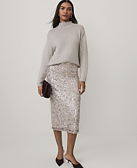 A woman wearing a grey sweater and a shimmering sequined skirt stands against a plain, light-colored background. carousel Product Image 2