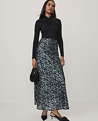A woman wearing a black long-sleeved top and a shimmering blue and silver sequined skirt stands against a plain, light-colored background. carousel Product Image 1