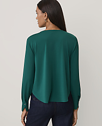 A woman wearing a dark green long-sleeved blouse and navy blue jeans stands against a plain, light-colored background. carousel Product Image 2