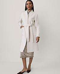 A woman wearing a long white belted coat over a sequined skirt and brown heels stands against a plain light grey background. carousel Product Image 1