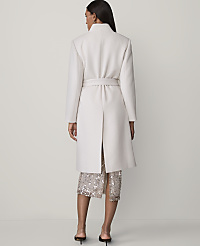 A woman stands with her back to the camera wearing a long white belted coat and a sequined skirt against a plain light grey background. carousel Product Image 2