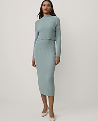 A woman wearing a light blue ribbed knit two-piece set and beige heels stands against a plain white background. carousel Product Image 1